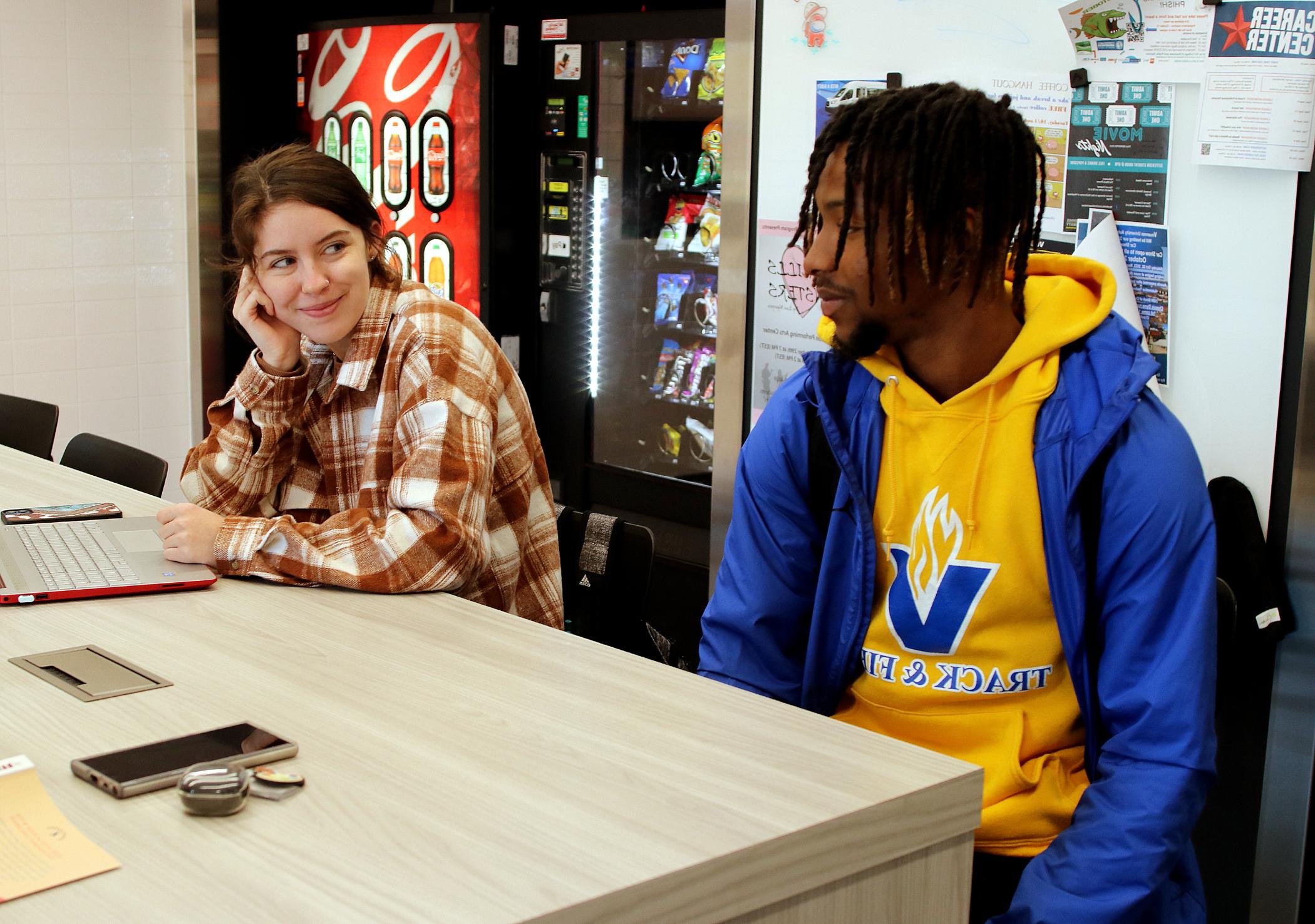 两个学生坐在自动售货机前的桌子旁
