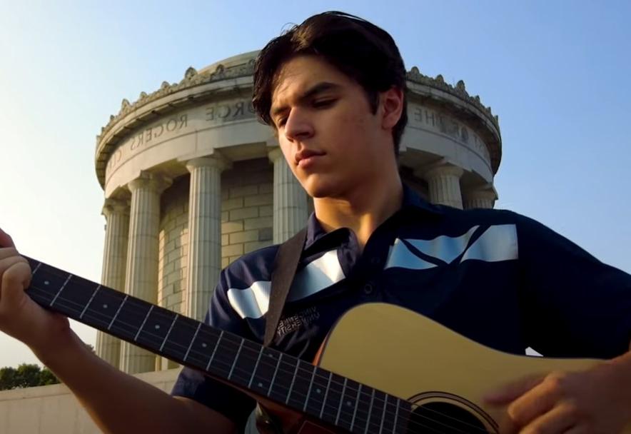 Male student playing a guitar in front of the George Rogers Clark memorial
