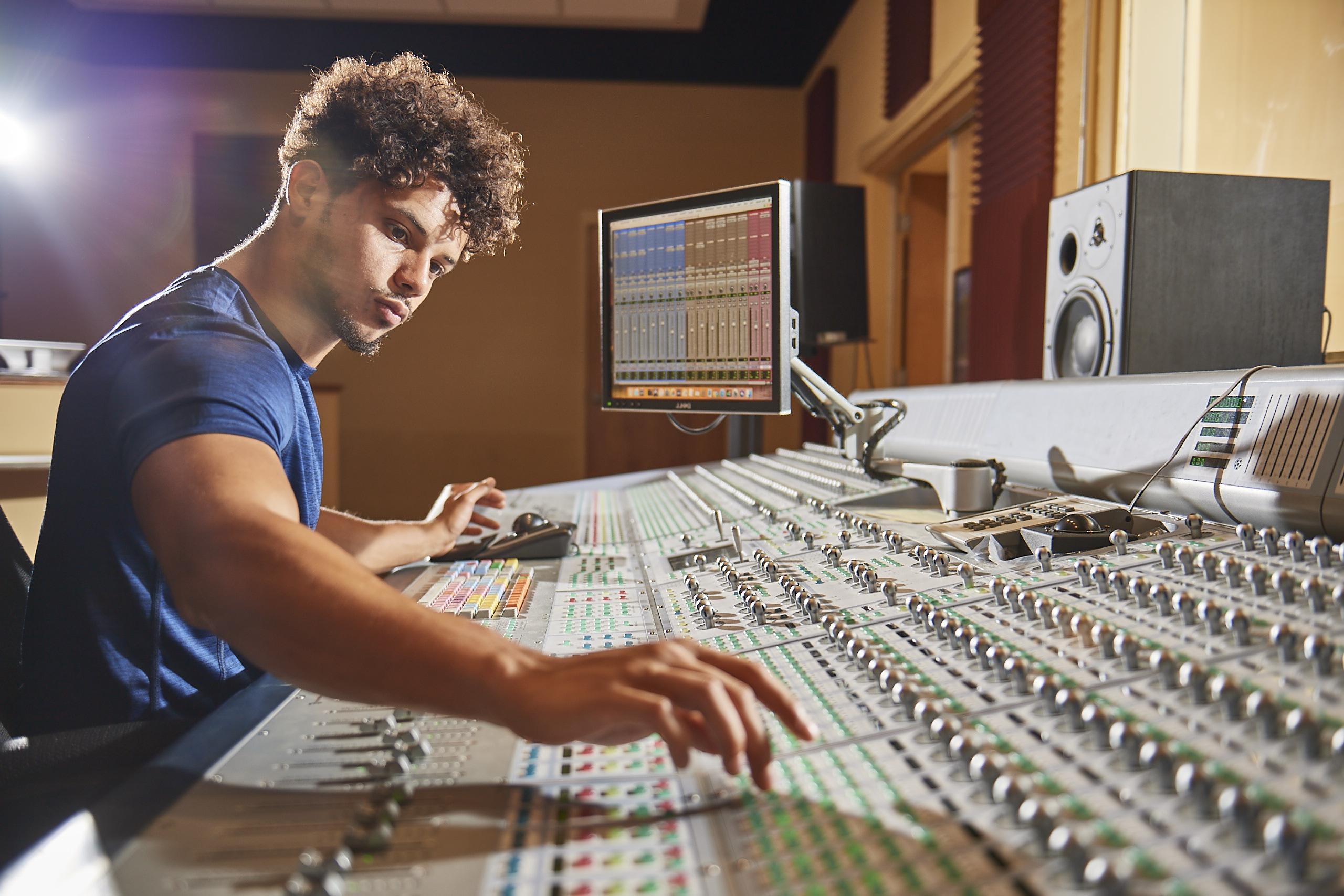 A male student adjusting some settings on a console in a recording studio